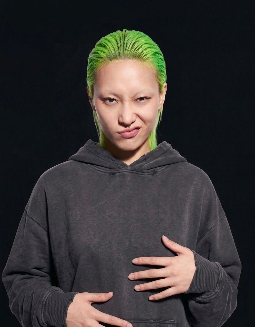 Person with bright green hair making a playful, slightly mischievous expression.