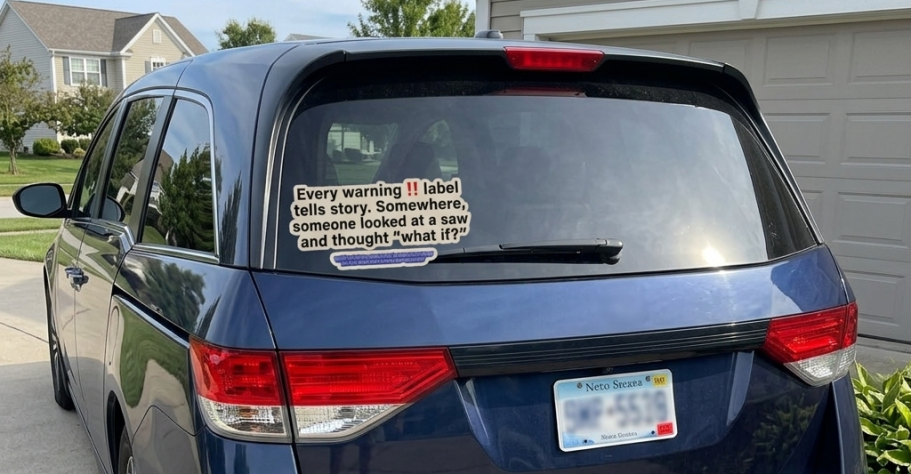 A blue minivan with a funny, sarcastic warning label sticker on the rear window.