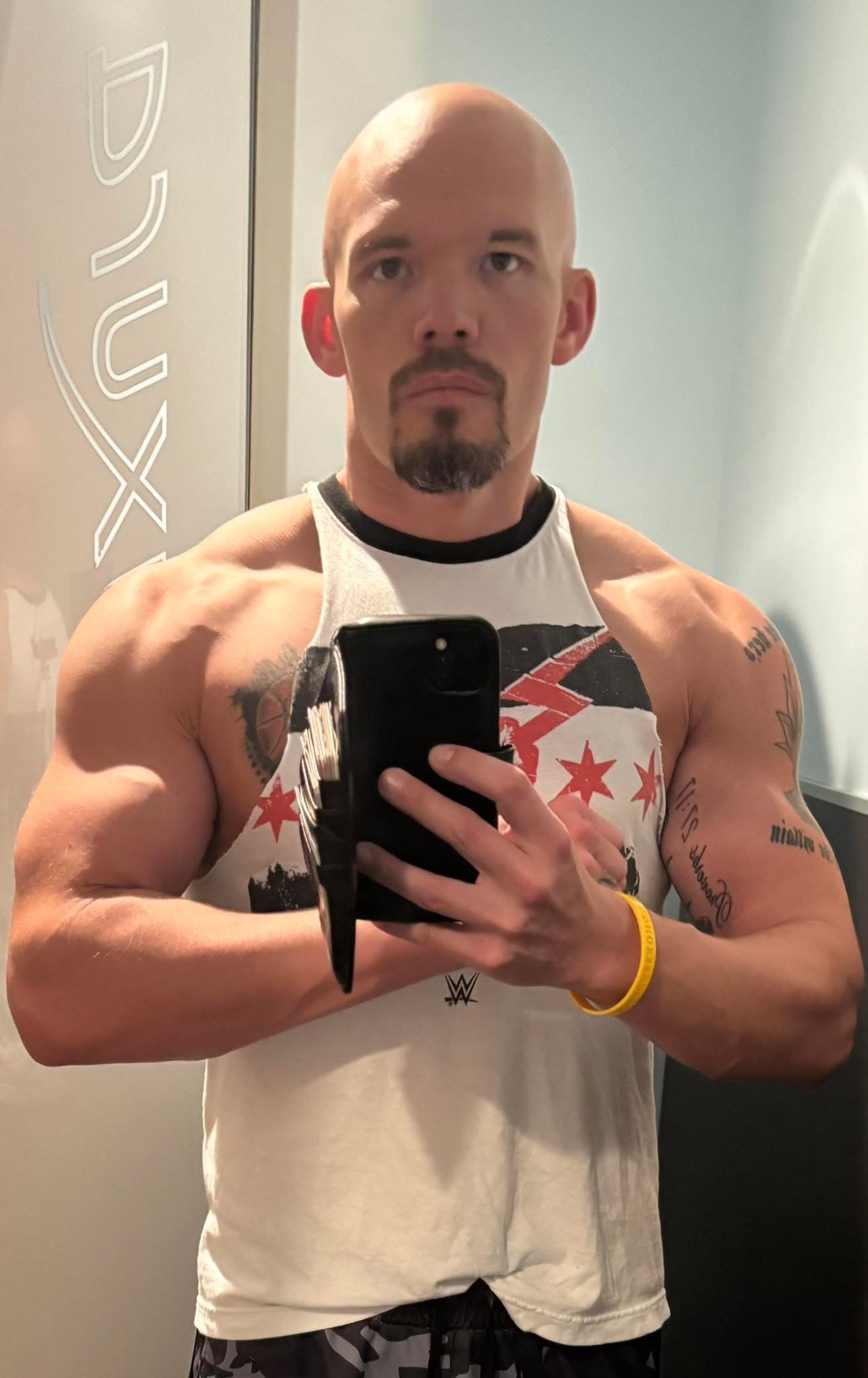 Alan “AJ” Foy Bald man in a tank top taking a selfie, showcasing muscular arms and a goatee.
